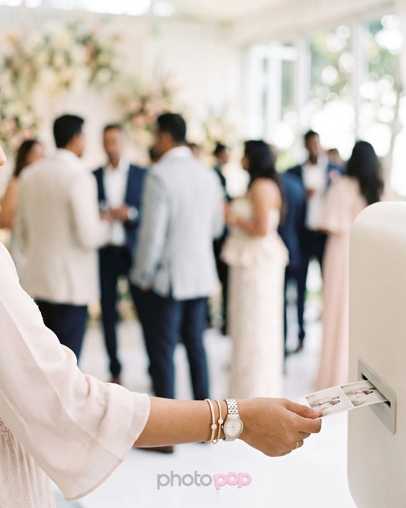Illustration: a guest in a blush dress collects a fresh photo strip from a white photo booth at a wedding reception
